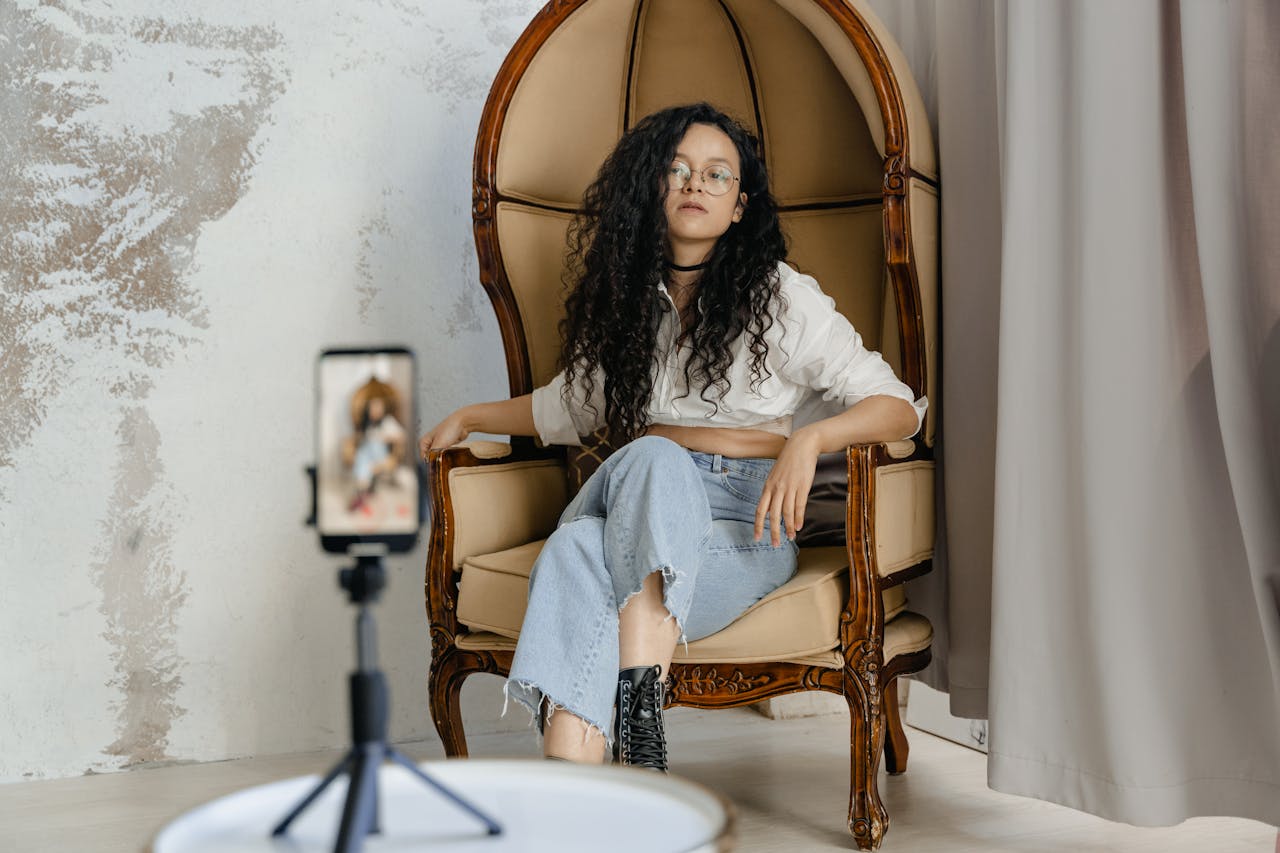 Stylish woman with curly hair taking a selfie indoors sitting on an ornate vintage chair.