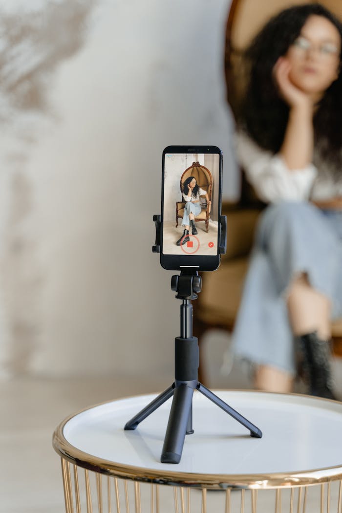 Young Asian woman filming content with smartphone on tripod indoors.