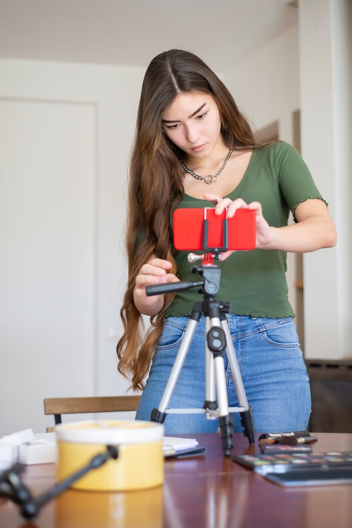 A young woman setting up a smartphone on a tripod in a modern home office environment.